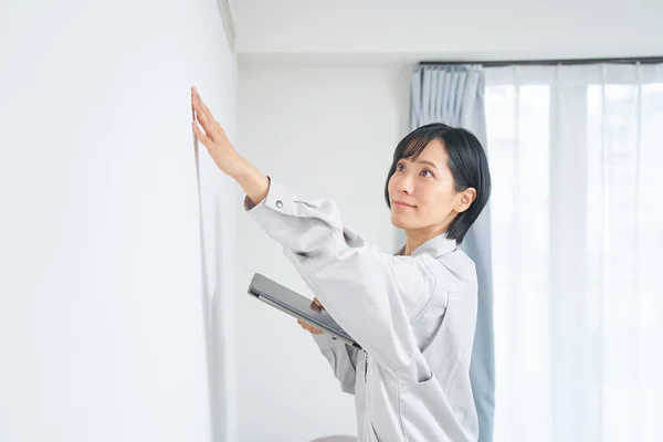 家の壁の状態を確認する作業服の女性 — ストック写真