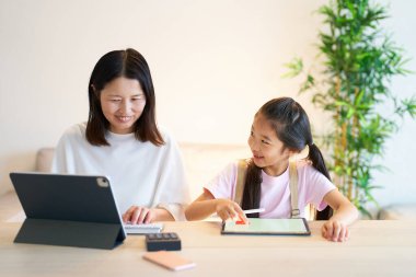 Evde tablet bilgisayar kullanan bir kadınla oynayan bir kız.