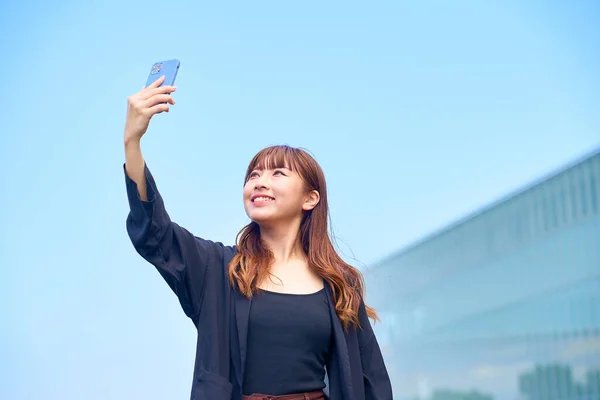 Mujer Joven Sosteniendo Teléfono Inteligente Bajo Cielo Azul —  Fotos de Stock