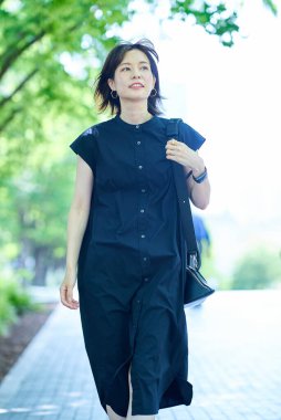 Genç bir kadın güzel bir günde ağaçlarla kaplı bir sokakta yürüyor.