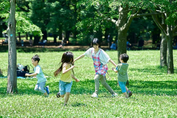 Μια Γυναίκα Ποδιά Και Παιδιά Παίζουν Κυνηγητό Στο Πάρκο — Φωτογραφία Αρχείου