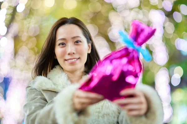 一个女人 晚上在户外拿着一个彩色包裹的礼物 — 图库照片