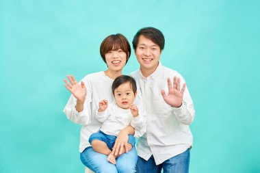 Gülümseyen bir aile mavi bir arka planın önünde ellerini sallıyor.