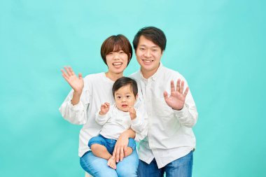 Gülümseyen bir aile mavi bir arka planın önünde ellerini sallıyor.