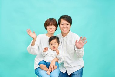 Gülümseyen bir aile mavi bir arka planın önünde ellerini sallıyor.