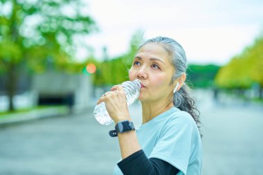Dışarıdaki plastik şişeden su içen yaşlı bir kadın.