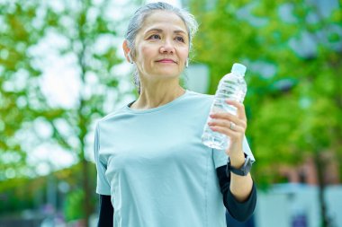 Dışarıdaki plastik şişeden su içen yaşlı bir kadın.