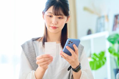 Odada elinde makbuz ve akıllı telefon tutan genç bir kadın var.