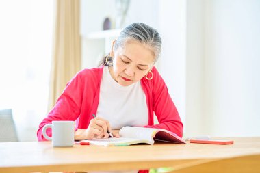 Oturma odasında kıdemli bir kadın ders çalışıyor.