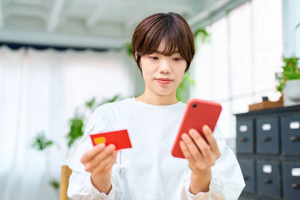 A woman holding a card and operating a smartphone indoors