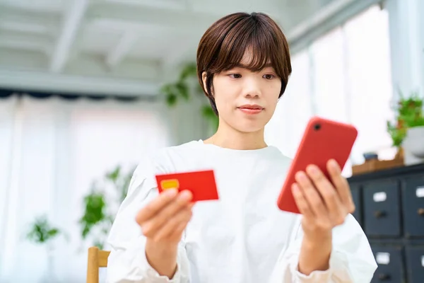 A woman holding a card and operating a smartphone indoors
