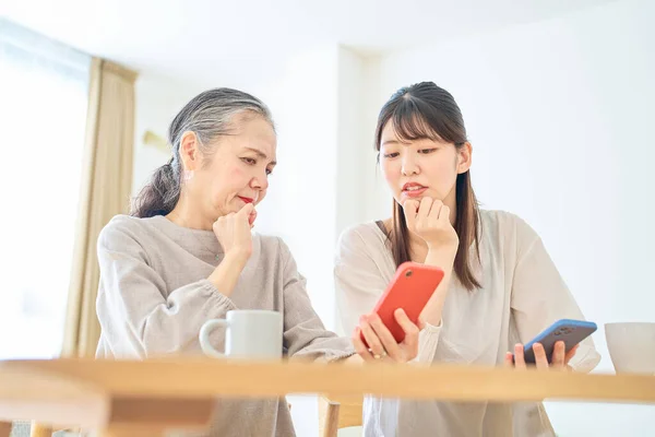 高齢の女性と若い女性は 屋内でスマートフォン画面を不安そうに見ています — ストック写真