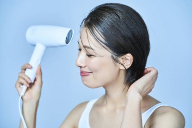 Saç kurutma makinesiyle saçını kurutan Asyalı kadın.