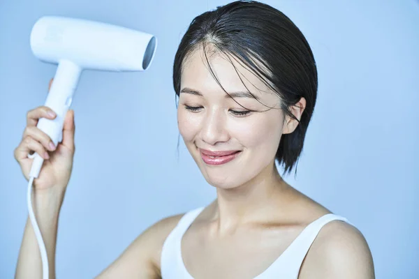 Asian woman drying her hair with a hair dryer