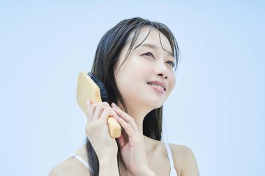 Uzun saçlı kadın gülümseyerek saçlarını tarıyor.