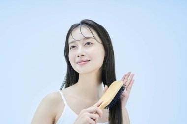 Uzun saçlı kadın gülümseyerek saçlarını tarıyor.