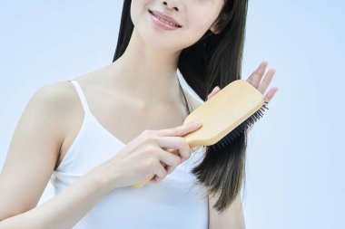 Uzun saçlı kadın gülümseyerek saçlarını tarıyor.