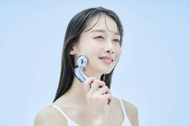 Genç bir kadın yüzüne masaj yapıyor ve soluk mavi bir geçmişi var.