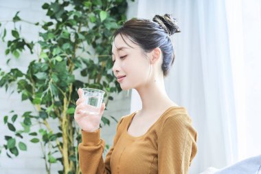 Pencerenin kenarında su içen genç bir kadın.