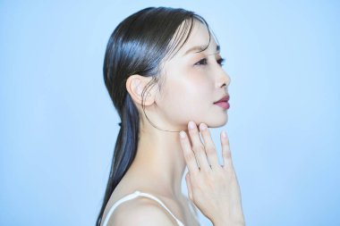 Genç bir kadın yüzüne dokunuyor ve soluk mavi arkaplan