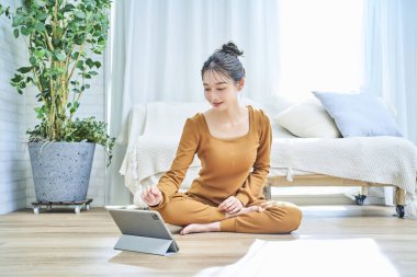 Loungewear giyen genç bir kadın tablet ekrana bakıyor.