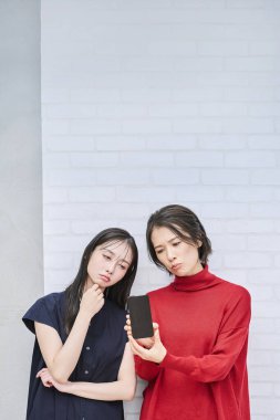 İki kadın endişeli bir ifadeyle akıllı telefonlarına bakıyor.