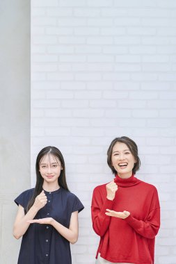 İki kadın gülümsüyor ve içeride inandırıcı bir şekilde poz veriyor.