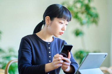 Odadaki bilgisayarla akıllı telefonu karşılaştıran genç bir kadın.