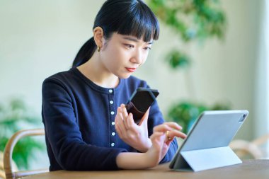 Odadaki bilgisayarla akıllı telefonu karşılaştıran genç bir kadın.