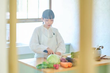 Mutfakta bıçakla malzeme kesen genç bir kadın.