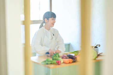 Mutfakta bıçakla malzeme kesen genç bir kadın.