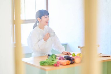 Mutfakta dinlenen genç bir kadın ve masada sıra olan sebzeler.