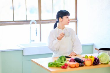 Mutfakta dinlenen genç bir kadın ve masada sıra olan sebzeler.