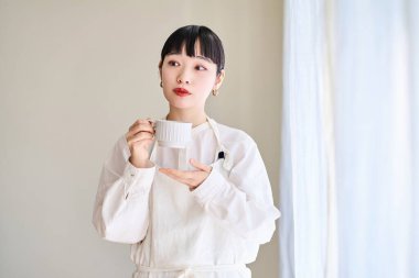 Önlüklü genç bir kadın odanın penceresinde mola veriyor.