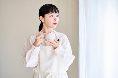 Önlüklü genç bir kadın odanın penceresinde mola veriyor.