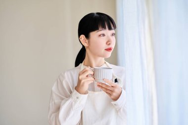 Önlüklü genç bir kadın odanın penceresinde mola veriyor.