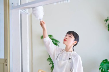 Odanın her köşesinden toz temizleyen genç bir kadın.