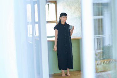 Genç bir kadın elinde kupayla odasında dinleniyor.