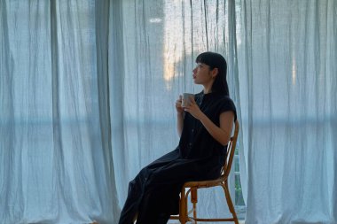 Gün batımında pencerenin kenarında dinlenen genç bir kadın.