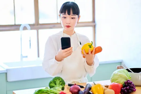 Молодая Женщина Собирает Овощи Смартфон Кухне — стоковое фото