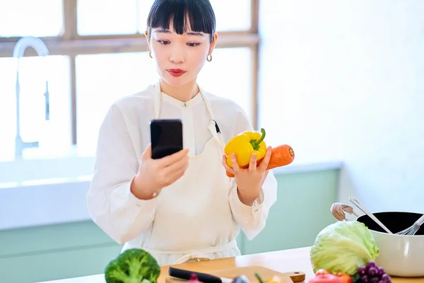 Mujer Joven Recogiendo Verduras Teléfonos Inteligentes Cocina —  Fotos de Stock