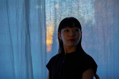 Gün batımında pencerenin kenarında dinlenen genç bir kadın.