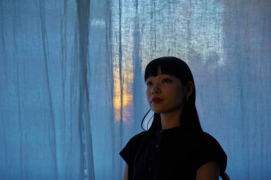 Gün batımında pencerenin kenarında dinlenen genç bir kadın.