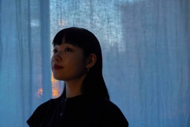 Gün batımında pencerenin kenarında dinlenen genç bir kadın.