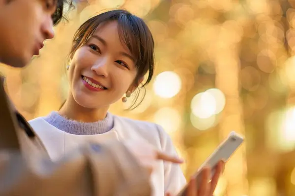 在一个灯火通明的城市 一个女人和一个男人快乐地使用智能手机 — 图库照片