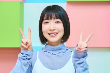 Genç kadın kameraya bakıyor ve barış işareti yapıyor.