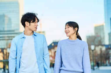 Genç adam ve kadın şehrin içinde yan yana yürüyorlar.