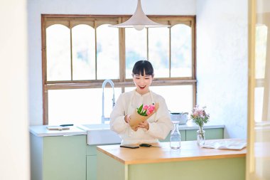 Odadaki vazoda çiçeklerin tadını çıkaran genç bir kadın.