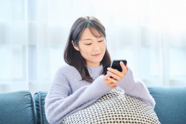 Odadaki akıllı telefon ekranına bakan genç bir kadın.