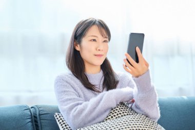 Odadaki akıllı telefon ekranına bakan genç bir kadın.